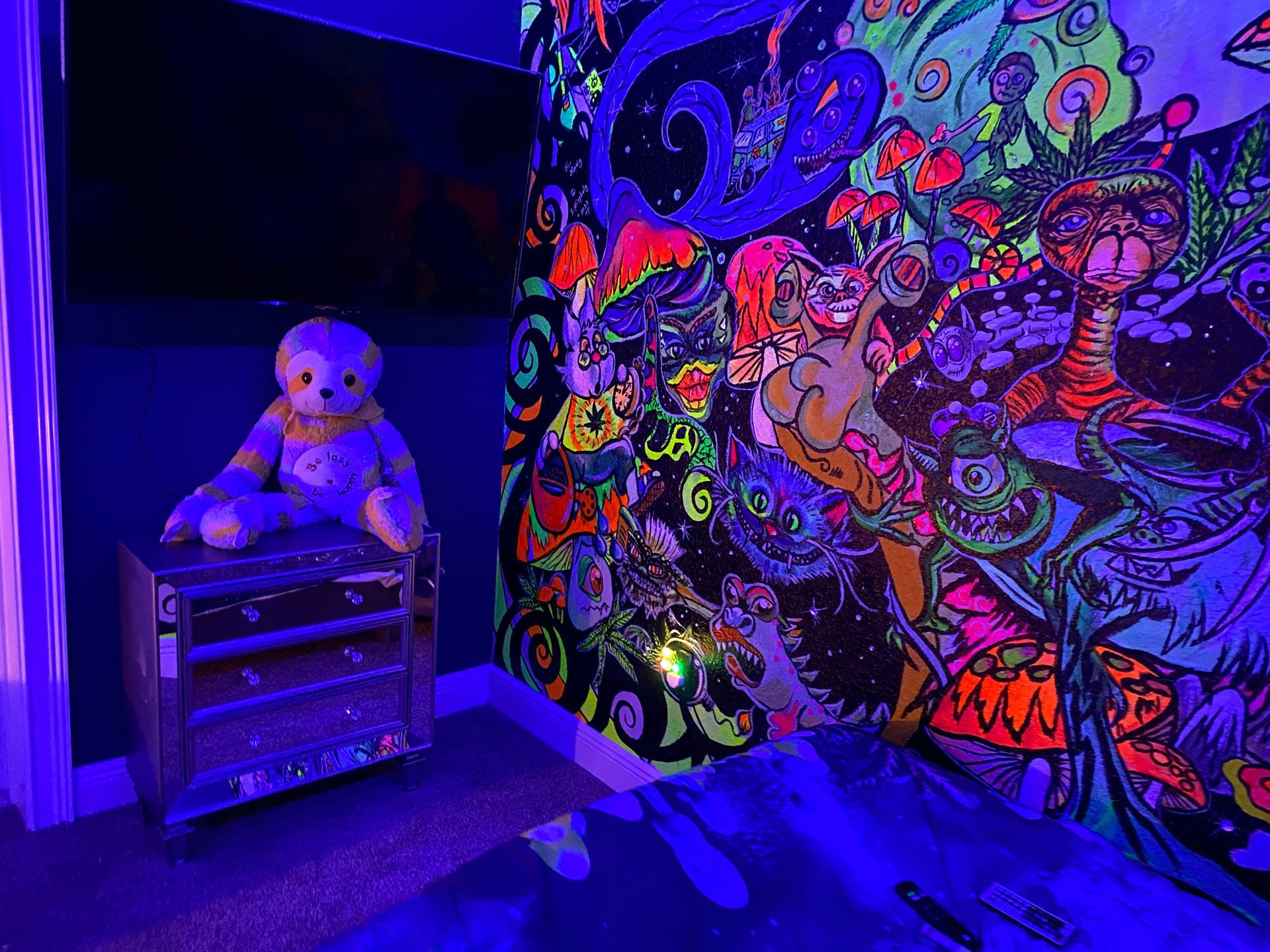Teddy bear on a cabinet beside a glowing neon graffiti mural in a blue-lit room