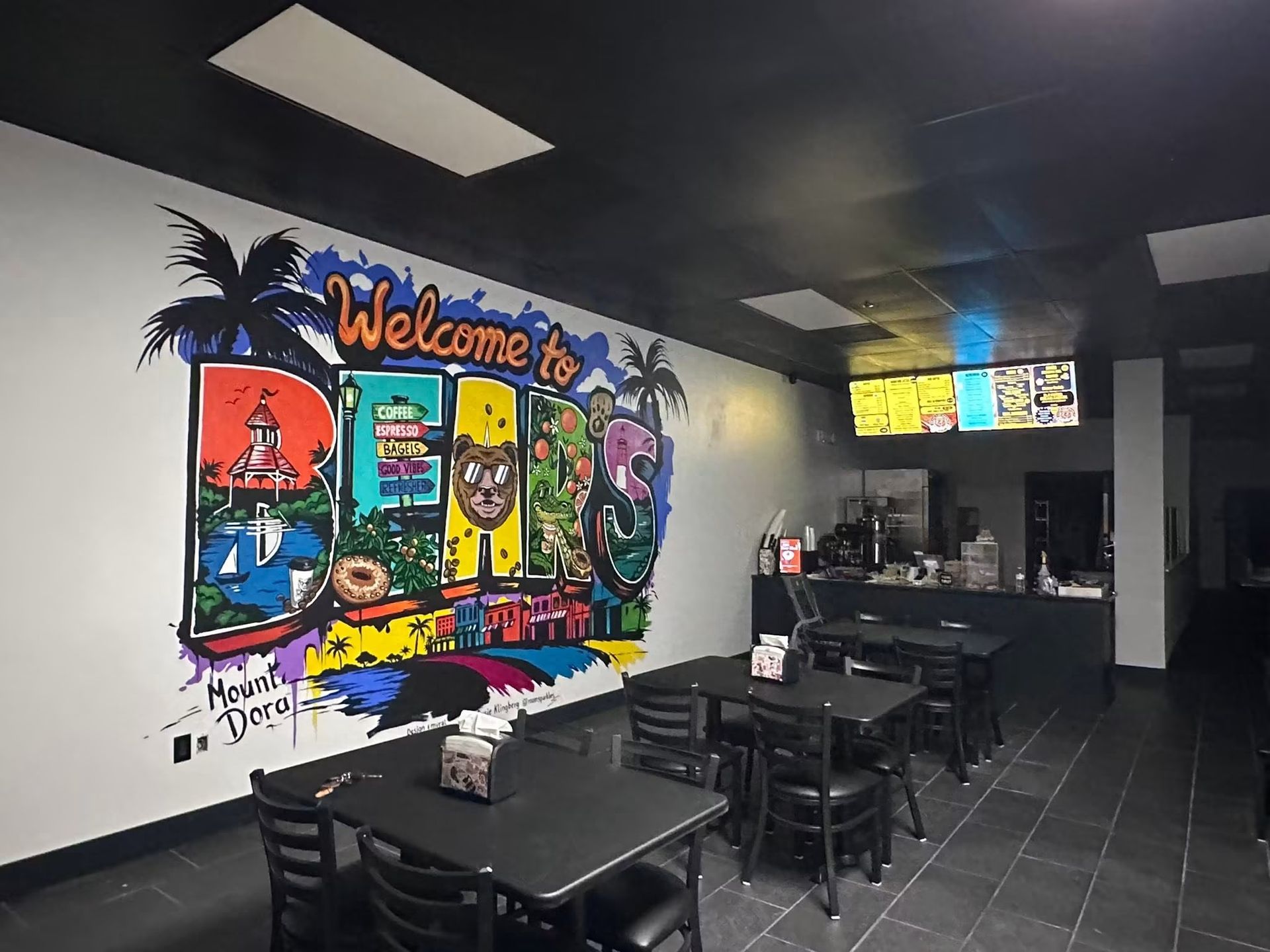 Colorful mural in a casual restaurant dining area with black tables and tiled floor
