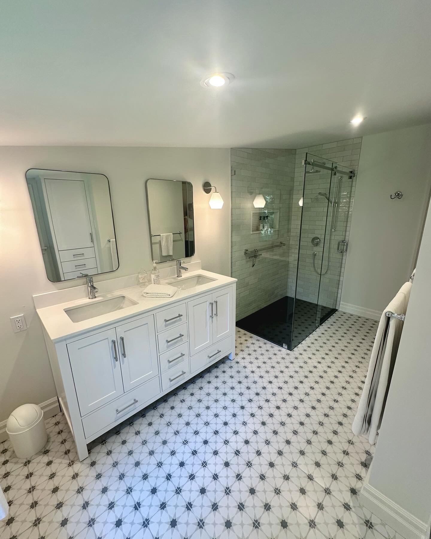 Modern bathroom with double vanity, walk-in shower, and patterned floor tiles.