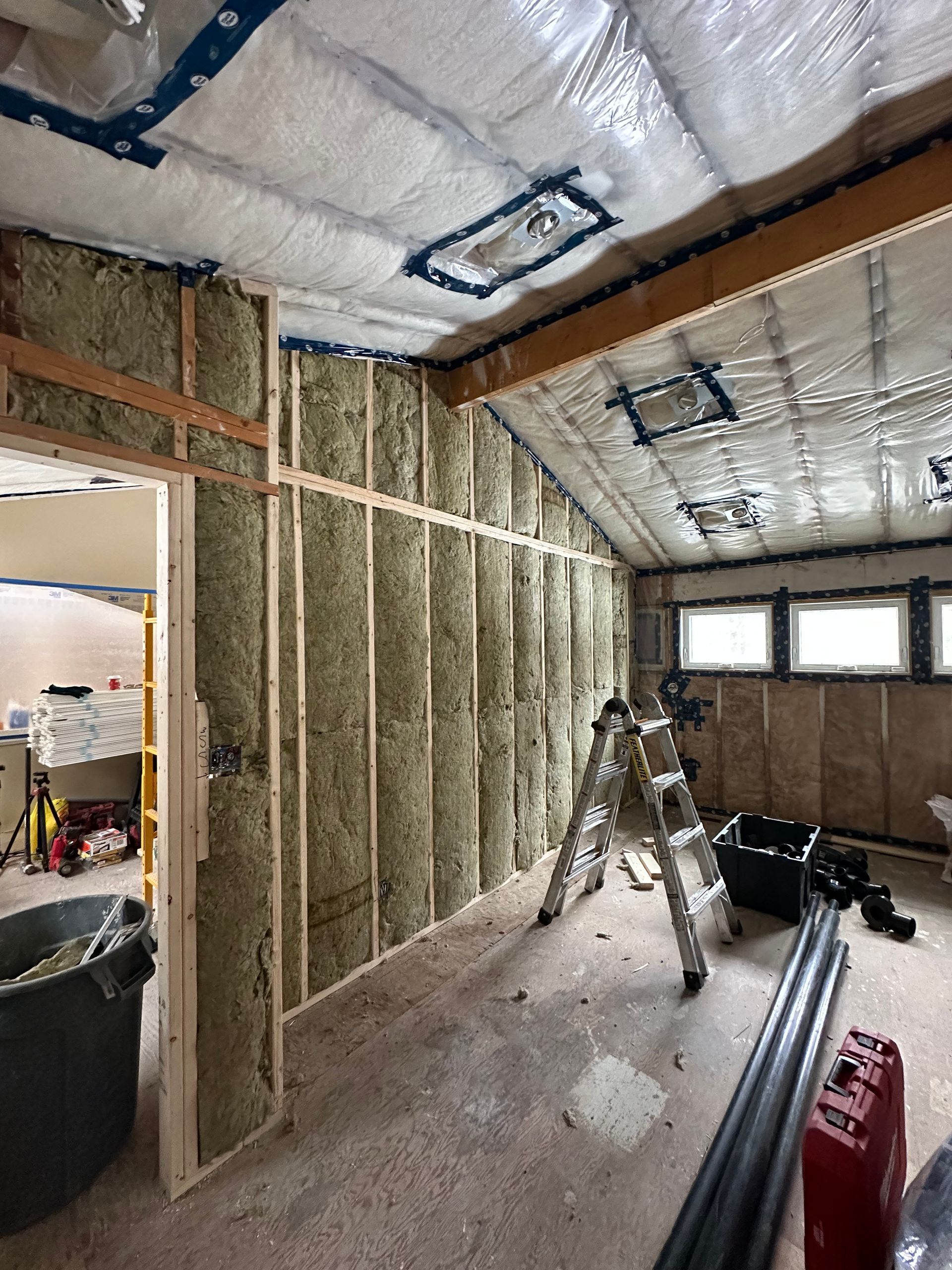 Interior of a room under construction, insulated walls and ceiling. A ladder and tools are visible.