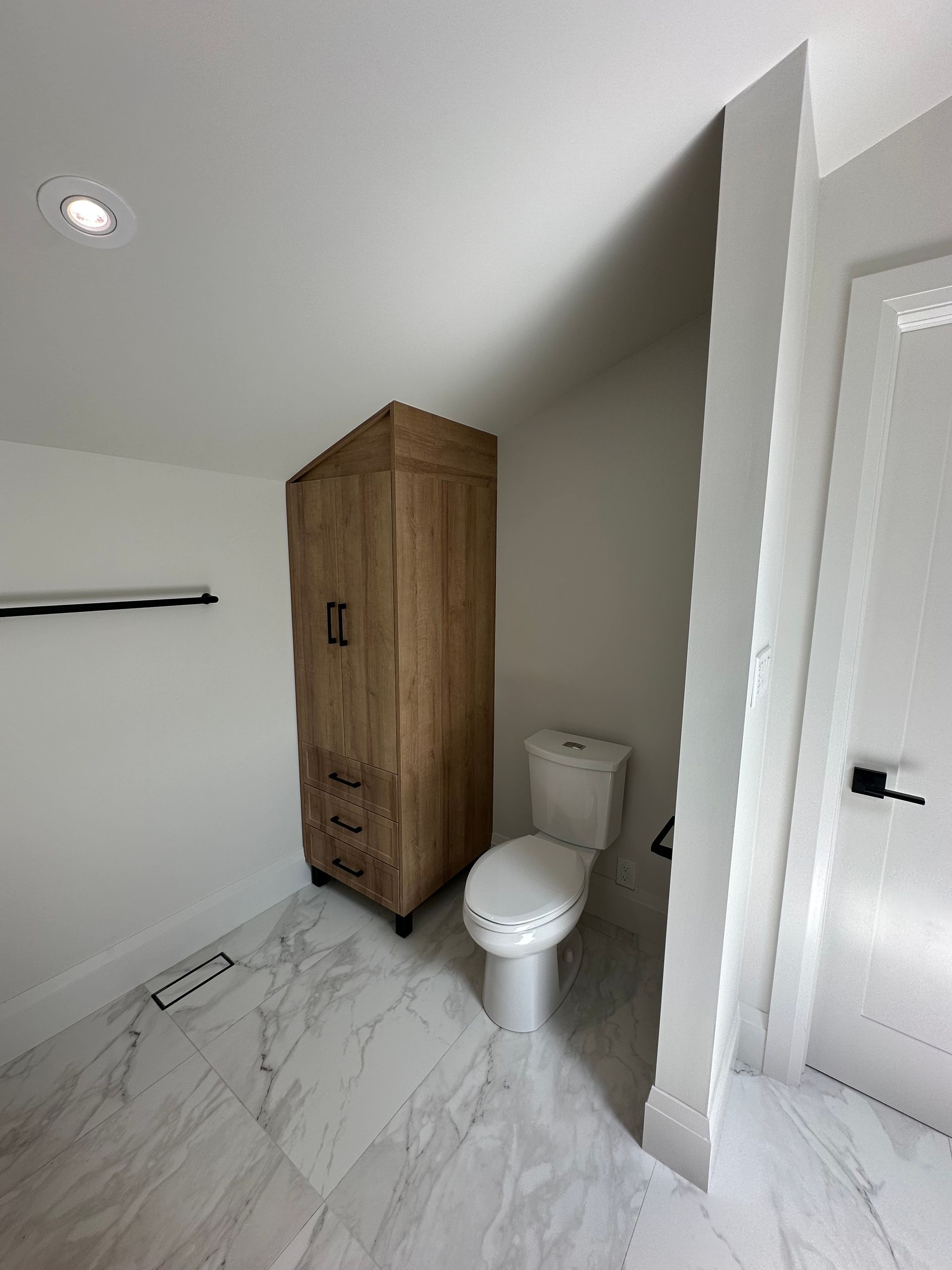 Bathroom with a wooden cabinet, toilet, and white door.