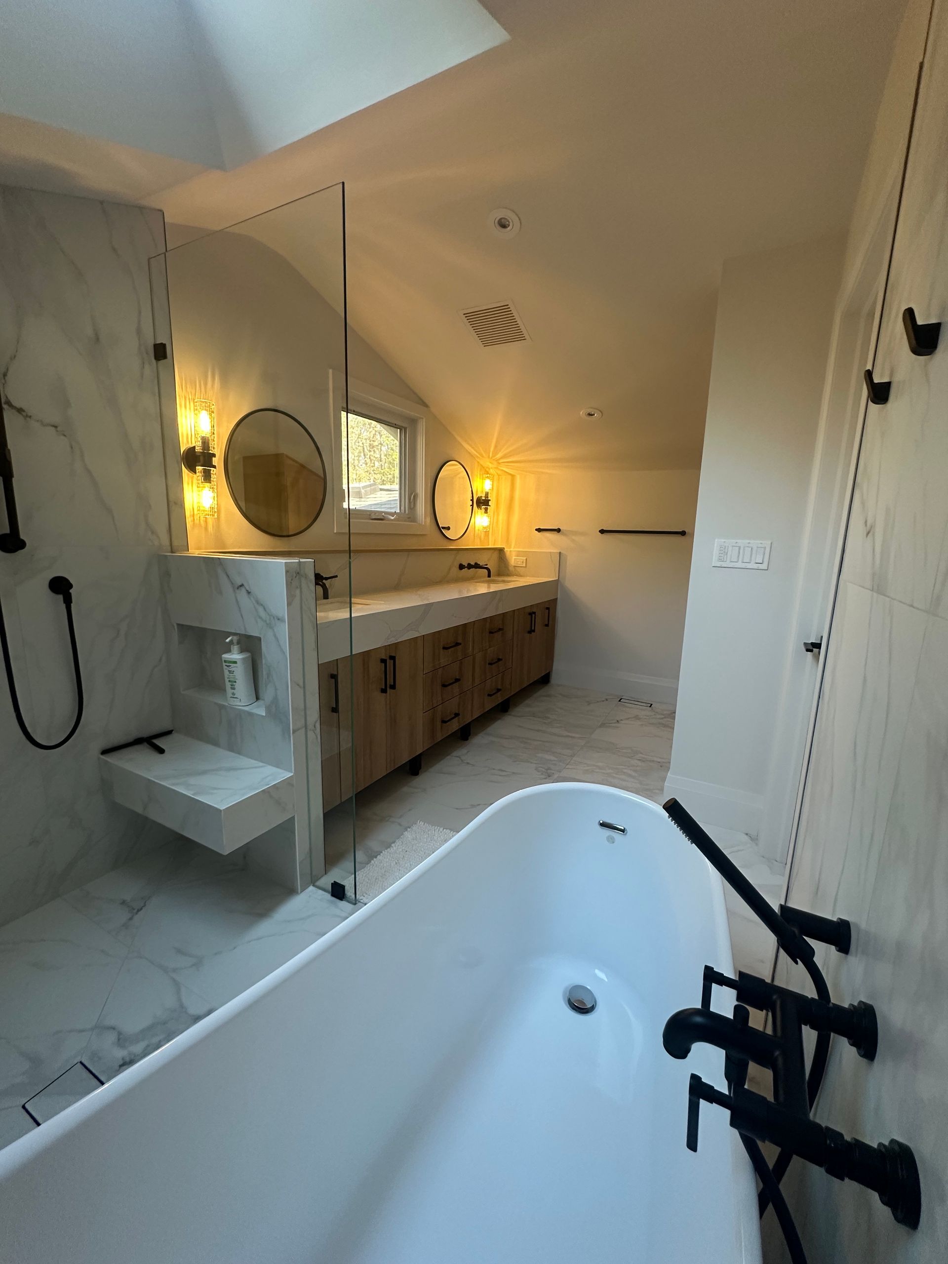 Spacious bathroom with a freestanding tub, marble shower, wooden vanity, and modern black fixtures.