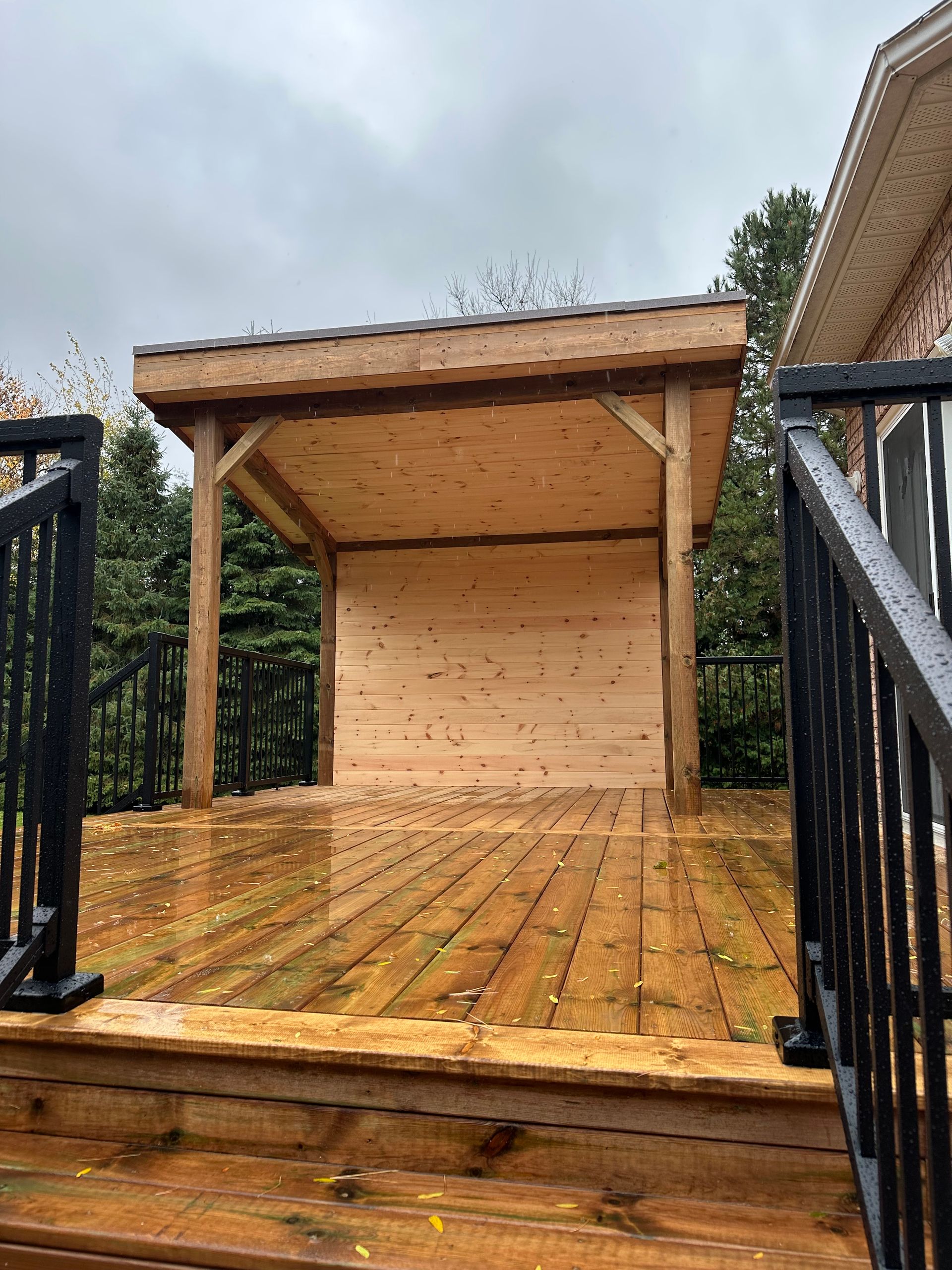 Wooden deck with a covered structure; black railings and a cloudy sky.