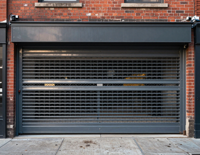 Closed gray storefront security shutter on a brick building with a sidewalk in front