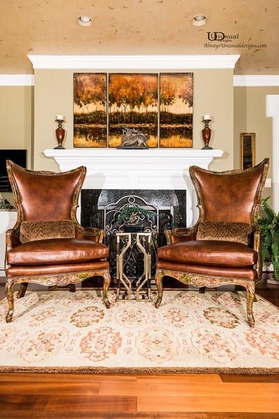 Two brown leather armchairs face a fireplace, flanked by a small table on a patterned rug.