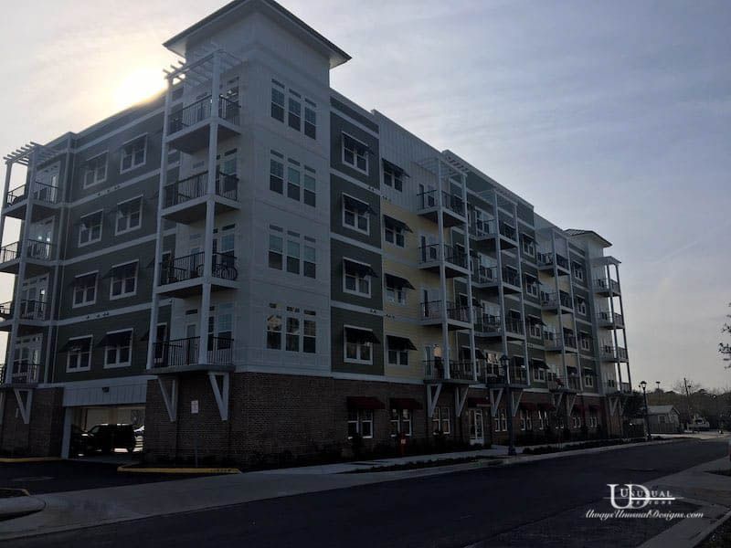 Multi-story apartment building with balconies, gray and yellow exterior, car parked in the garage.