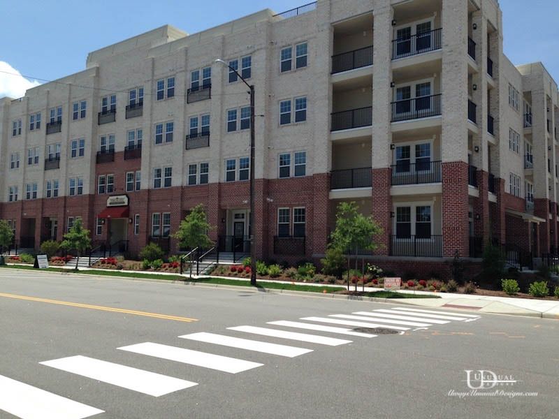 Multi-story apartment building with tan and red brick exterior, balconies, and a crosswalk in the foreground.