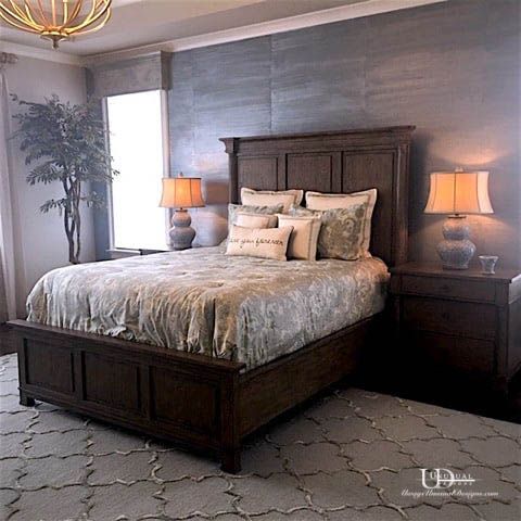 Bedroom with dark wooden bed, nightstands, lamps, and a patterned rug. Gray textured wall behind the bed.
