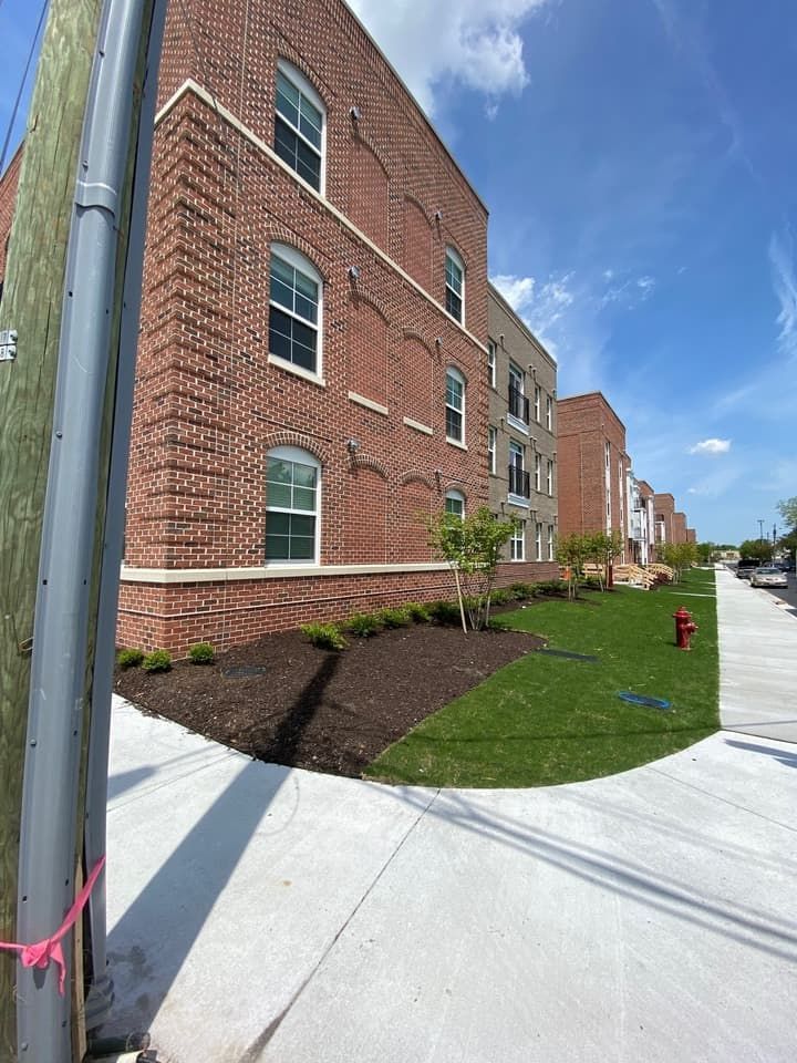 Brick apartment building with green lawn, sidewalk, and utility pole against a blue sky.
