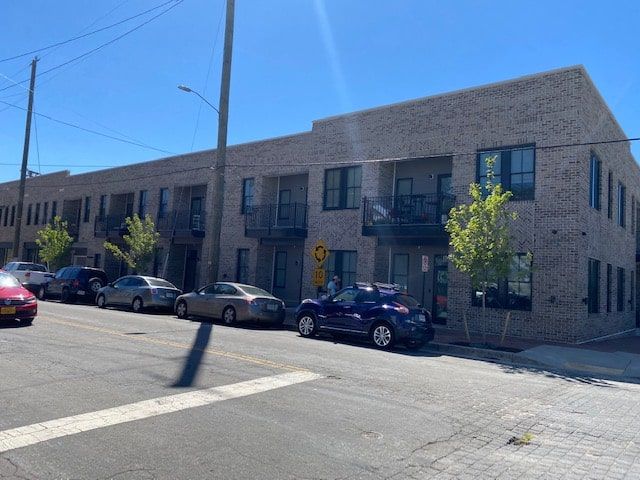 Brick apartment building on a street with parked cars and a clear blue sky.