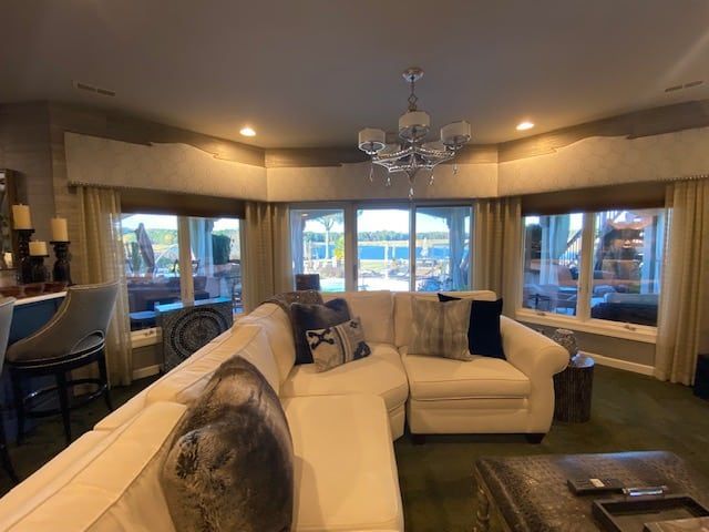 Living room with a white sectional sofa, large windows overlooking a lake, and a chandelier.