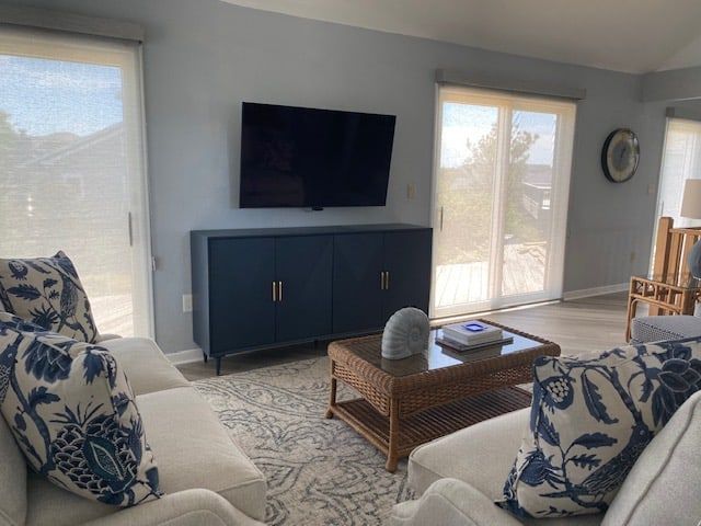 Living room with blue accents: TV on blue cabinet, beige couch with blue floral pillows, wicker coffee table, and large windows.