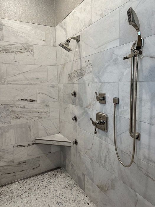 Marble-tiled shower with a bench seat and multiple shower heads, including a handheld wand.