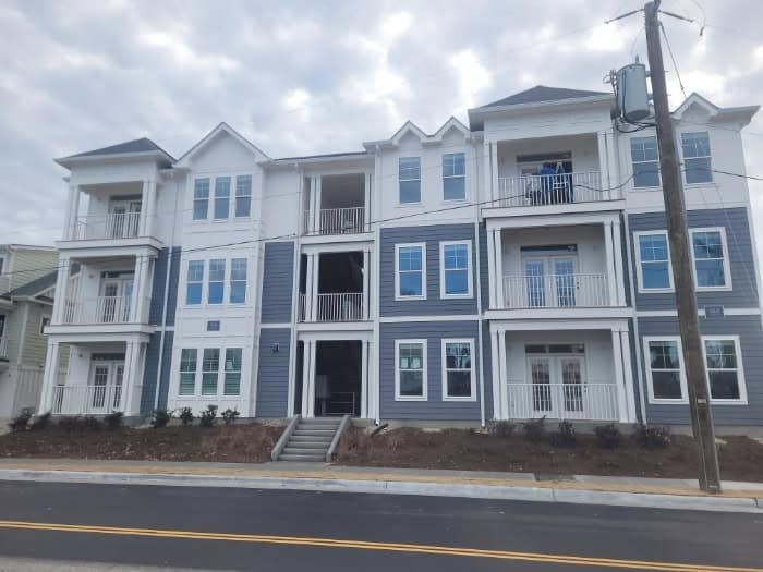 Multi-story apartment building under construction, featuring white and blue siding, balconies, and large windows.