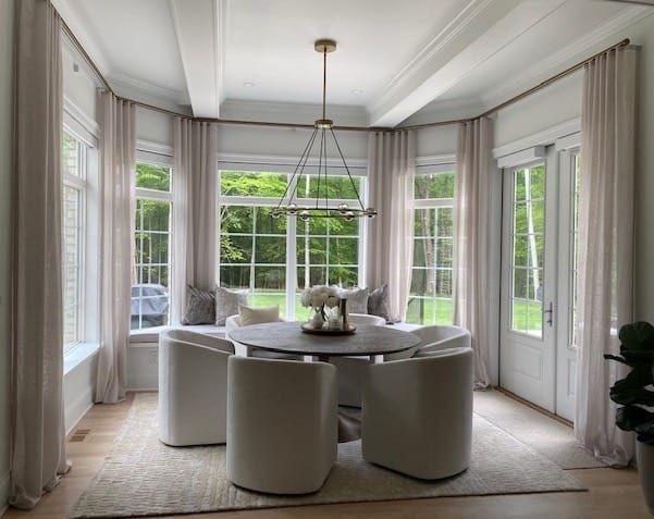 Dining room with round table, white chairs, and large windows with cream curtains.