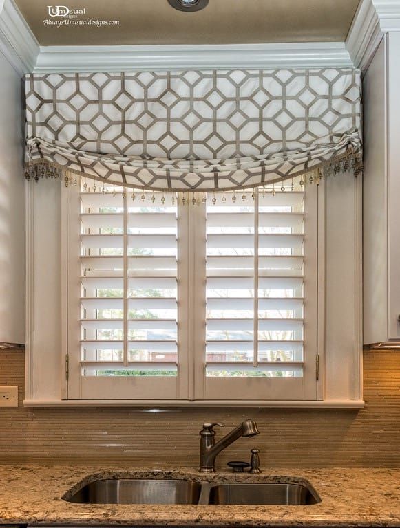 Kitchen window with white shutters, a patterned valance, and a sink.