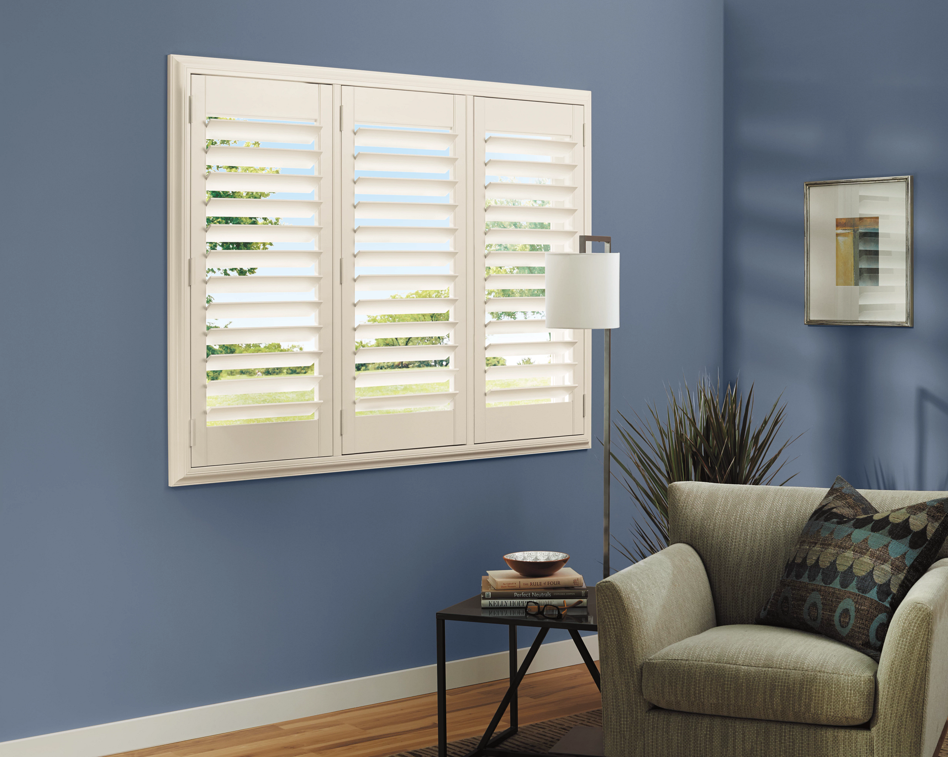 Cream-colored shutters on a blue wall. An armchair, lamp, and side table complete the room.
