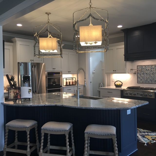 Kitchen with white cabinets, blue island with stools, two pendant lights, and stainless steel appliances.