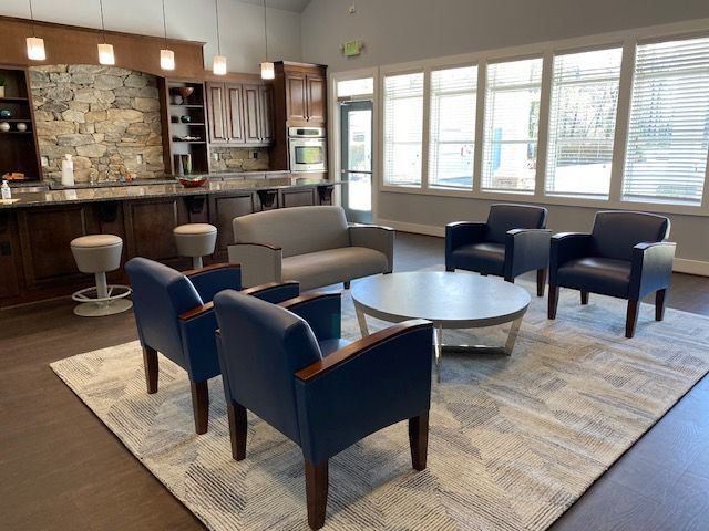 Lounge area with blue armchairs, a gray sofa, a round coffee table on a patterned rug, and a bar with stone wall.