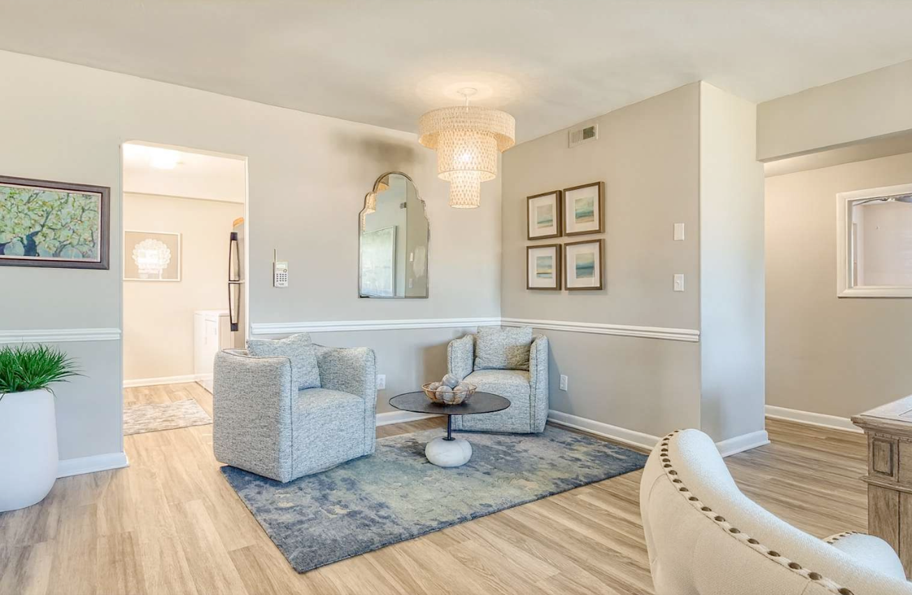 Living room with light gray walls, two armchairs, rug, and crystal chandelier.