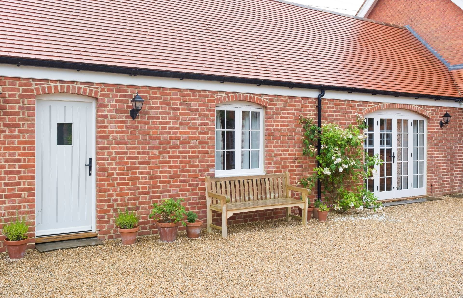 Brick cottage with white door, windows, and bench; red tiled roof.