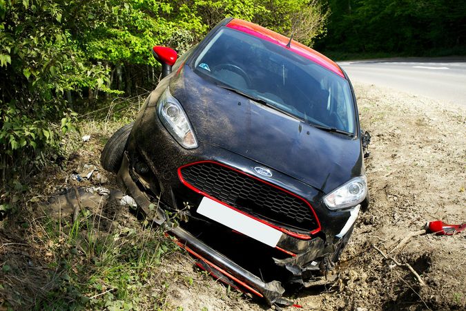 A black and red car is stuck in the mud on the side of the road.