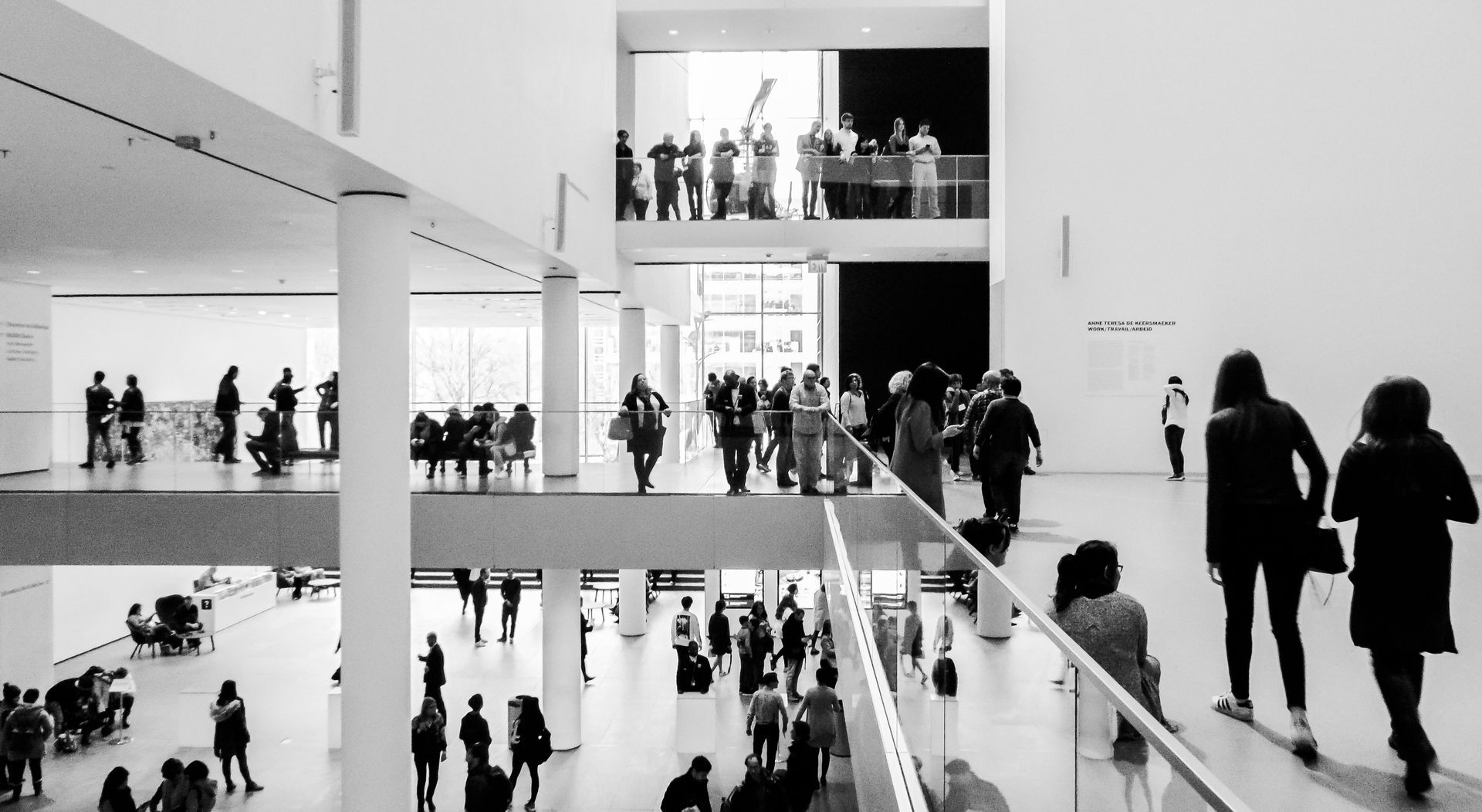 Een druk interieur van een museum voor moderne kunst, met mensen die op de boven- en benedenverdiepingen rondlopen.