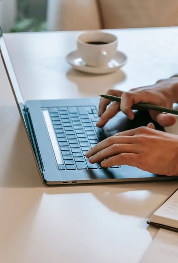 Handen typen op een laptop naast een kop koffie op een wit bureau.