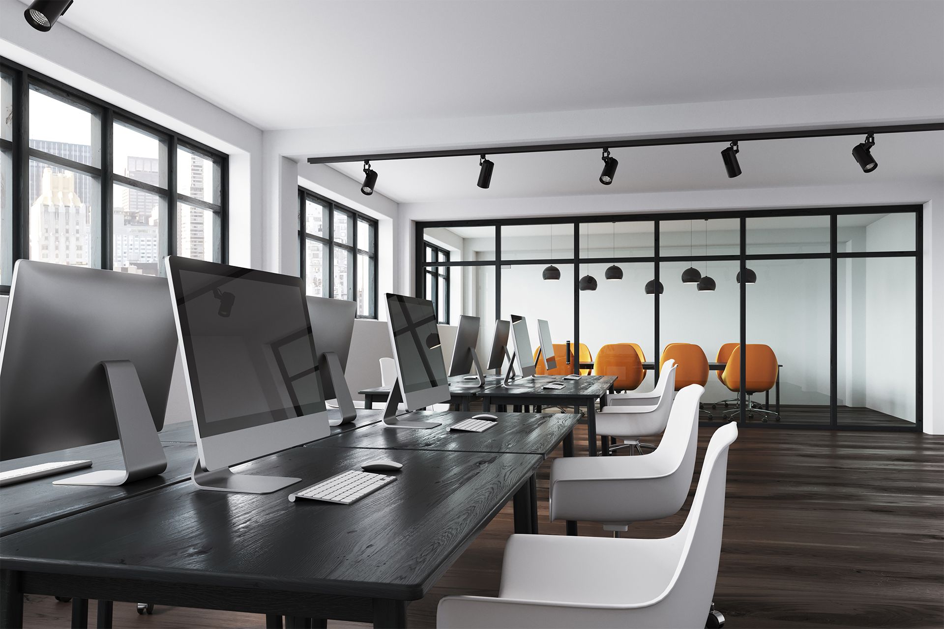 Modern office space with dark desks, computers, white chairs, and a glass-walled conference room with orange chairs.