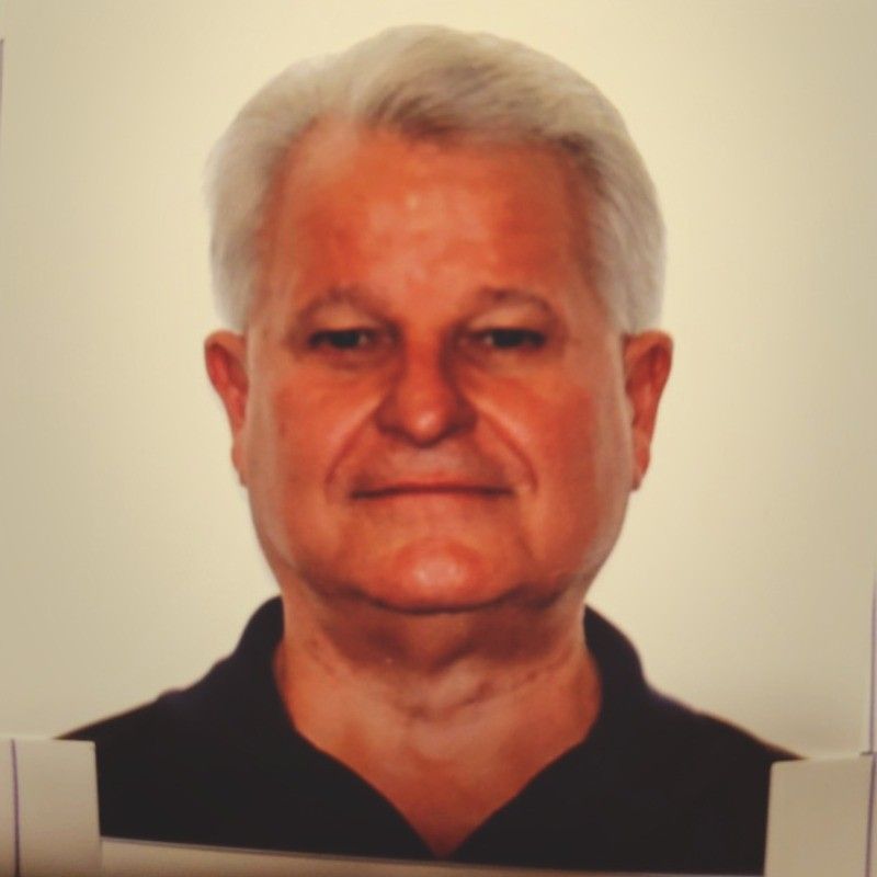 Smiling man in a gray shirt standing indoors with vehicle posters in the background