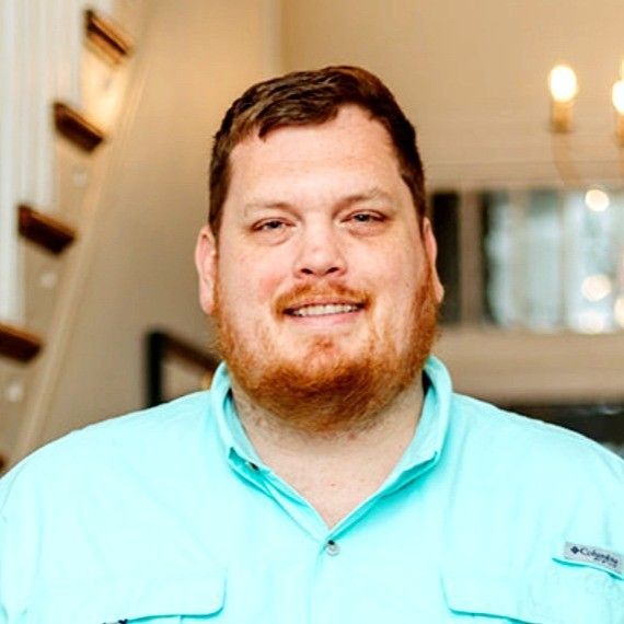 Smiling man in a gray shirt standing indoors with vehicle posters in the background