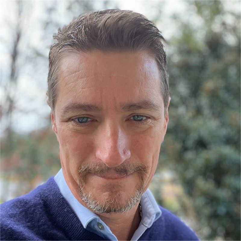 Portrait of a smiling person wearing glasses and a beard on a gray background