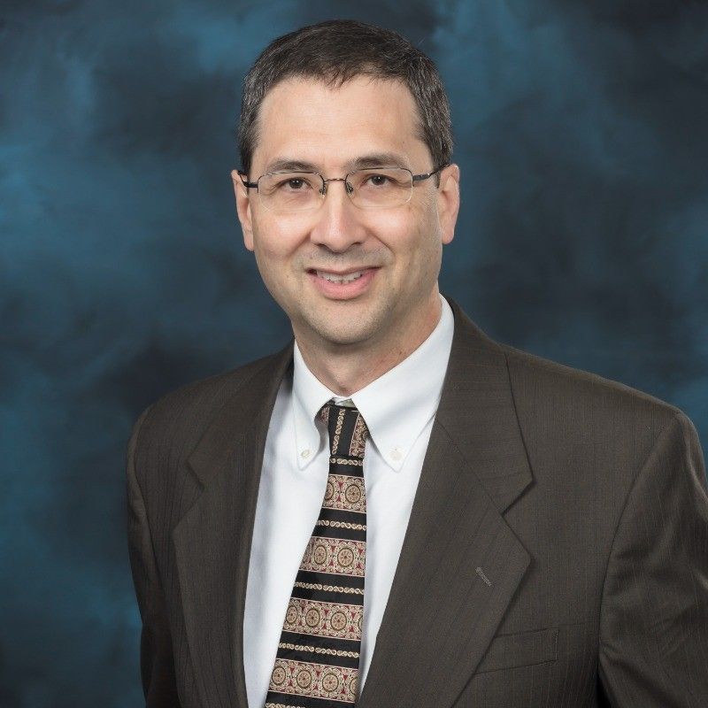 Smiling man in a navy plaid suit jacket and striped shirt on a white background