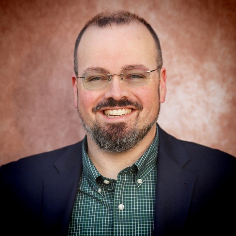 Smiling man in a navy plaid suit jacket and striped shirt on a white background