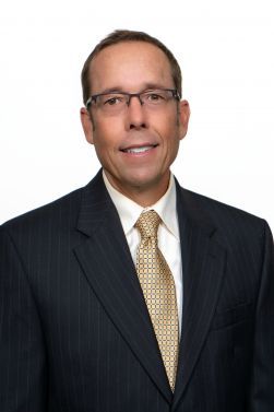 Headshot of a smiling person with glasses against a blue background
