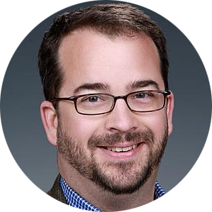 Portrait of a smiling person wearing glasses and a beard on a gray background