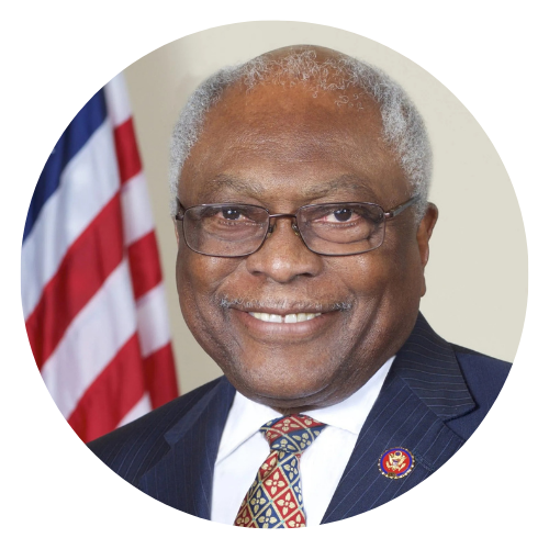 Smiling man in a navy suit and glasses, with a U.S. flag in the background