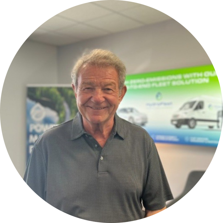 Smiling man in a gray shirt standing indoors with vehicle posters in the background