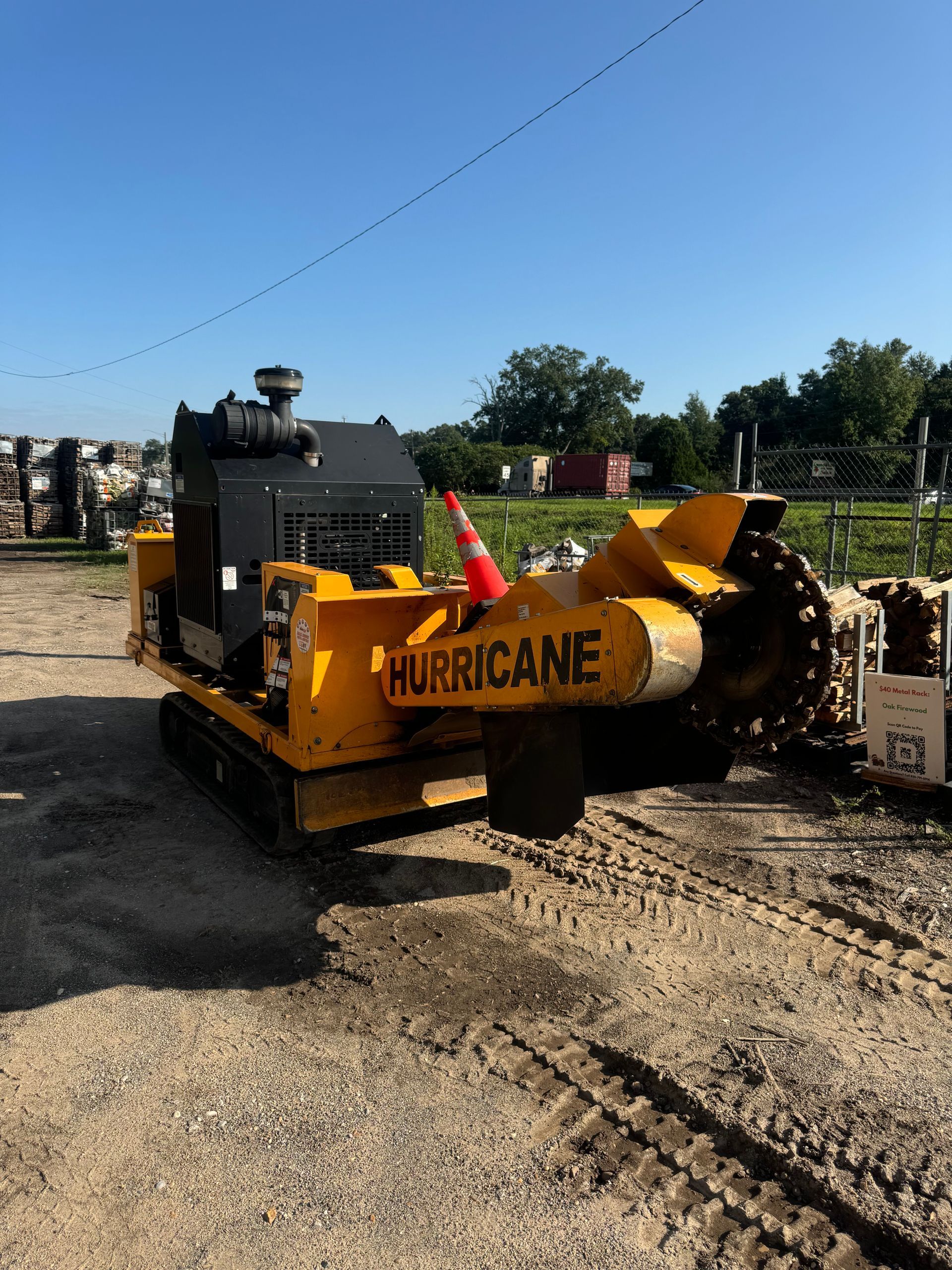 A yellow hurricane stump grinder is parked in a dirt lot.