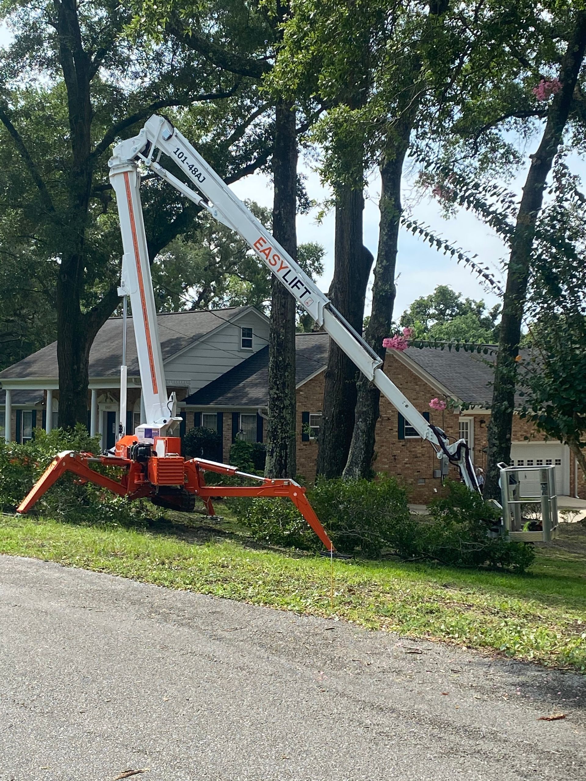 A crane is cutting a tree in front of a house.
