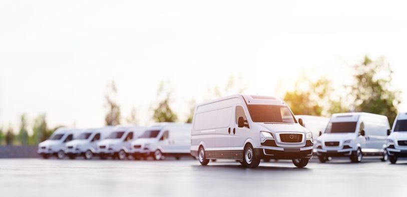 a row of white vans are parked in a parking lot .