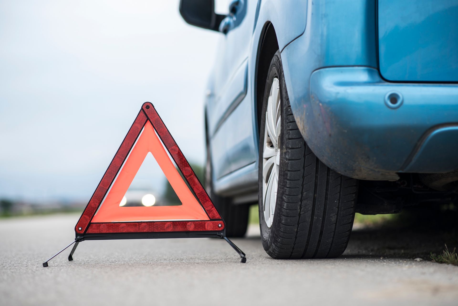 Emergency warning triangle behind broken-down blue car on roadside highlighting vehicle safety tips.