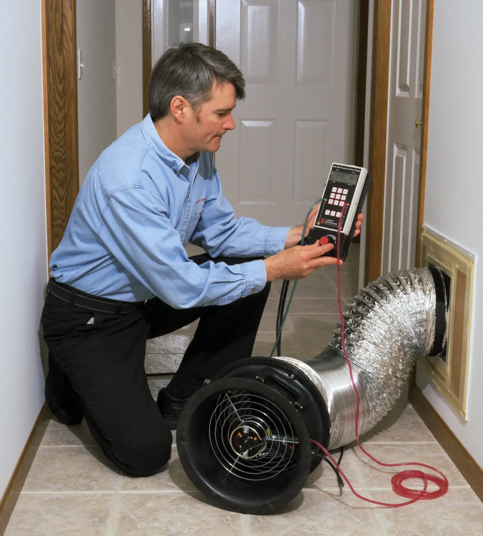 A man in a blue shirt is kneeling down next to a fan