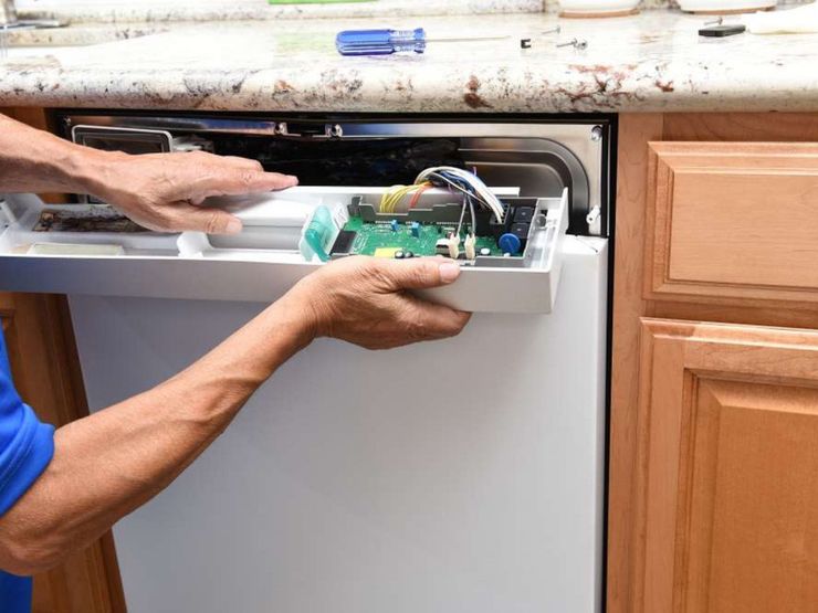 Person installing a dishwasher under a kitchen counter with the front panel removed