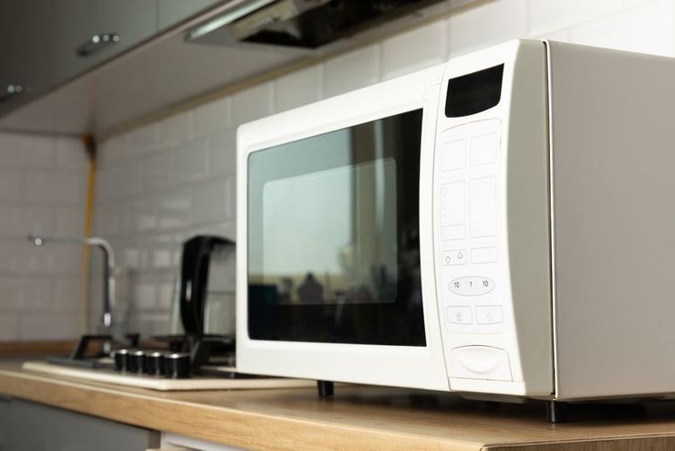 White microwave on a kitchen counter with tiled backsplash and sink in the background