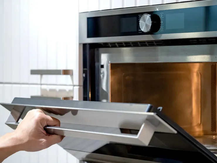 Hand placing a metal tray into a stainless steel oven in a modern kitchen