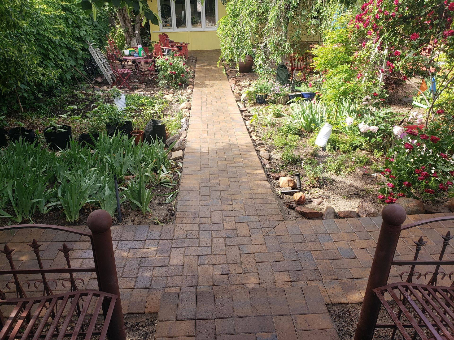 Brick garden path leading through lush flower beds to a house