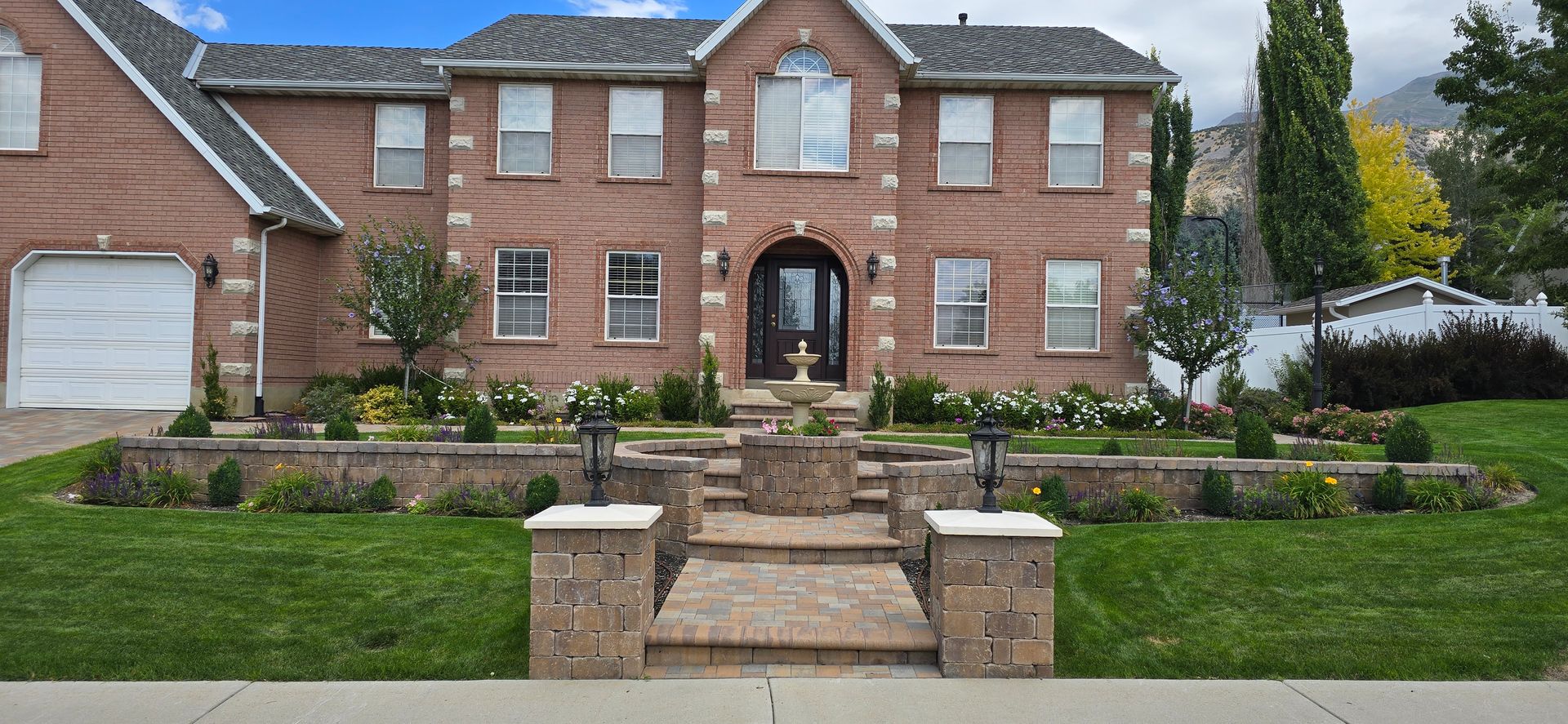 Brick suburban house with stone steps, front walkway, lawn, and flower beds