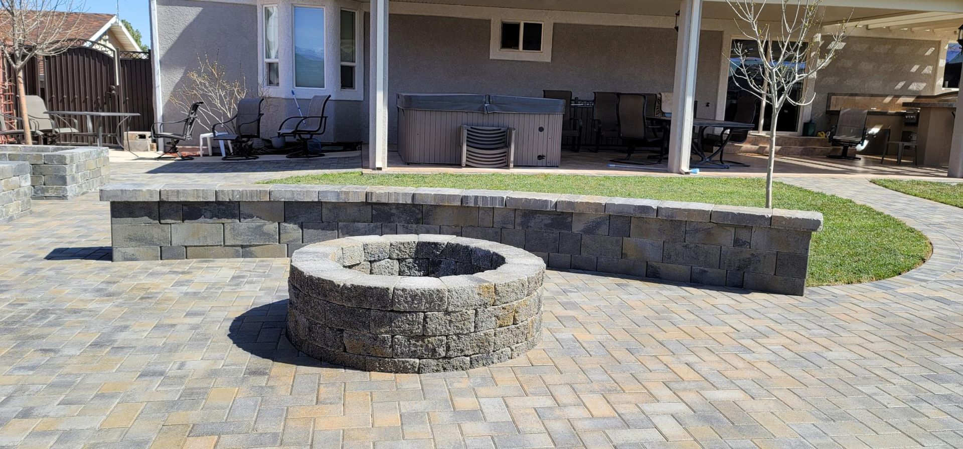 Stone fire pit and curved bench seating in a paved backyard patio with a covered porch.
