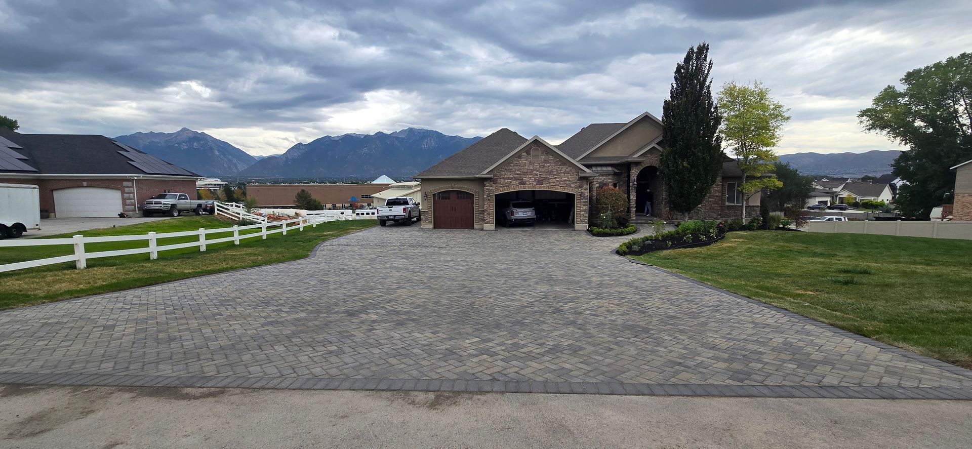 Gravel driveway leading to a brick suburban house with mountains in the background under cloudy skies